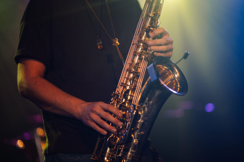 Saxophonist playing sax on stage during concert under colorful lights